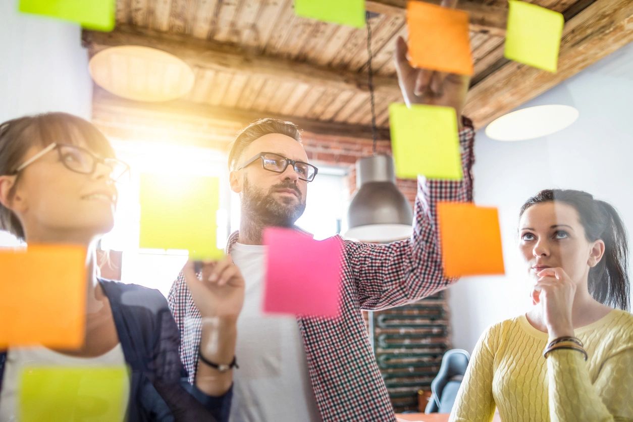 People mapping the sales funnel stages and keywords on a glass whiteboard using sticky notes